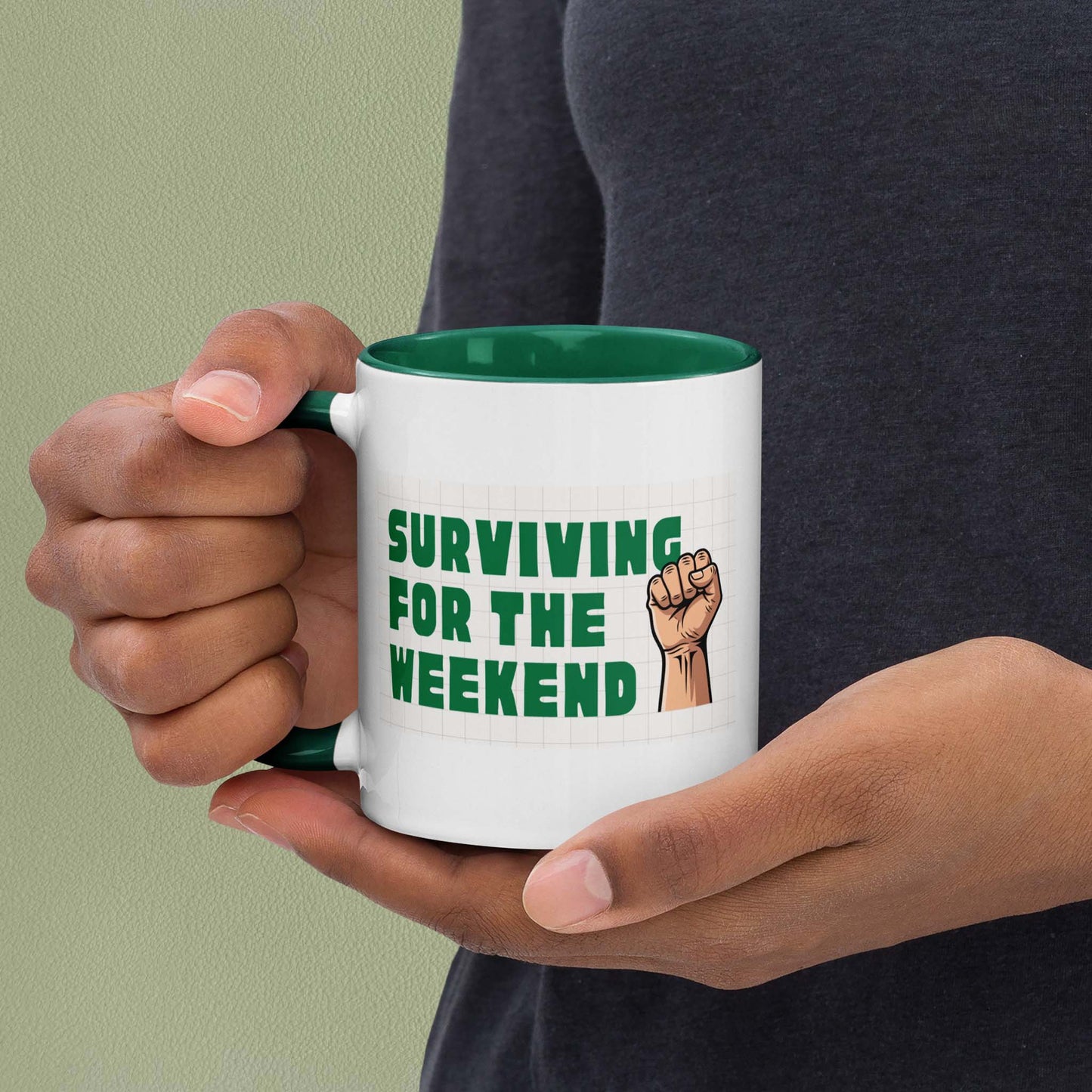 White ceramic mug with green interior reading 'Surviving for the weekend' in bold green text with a raised fist illustration
