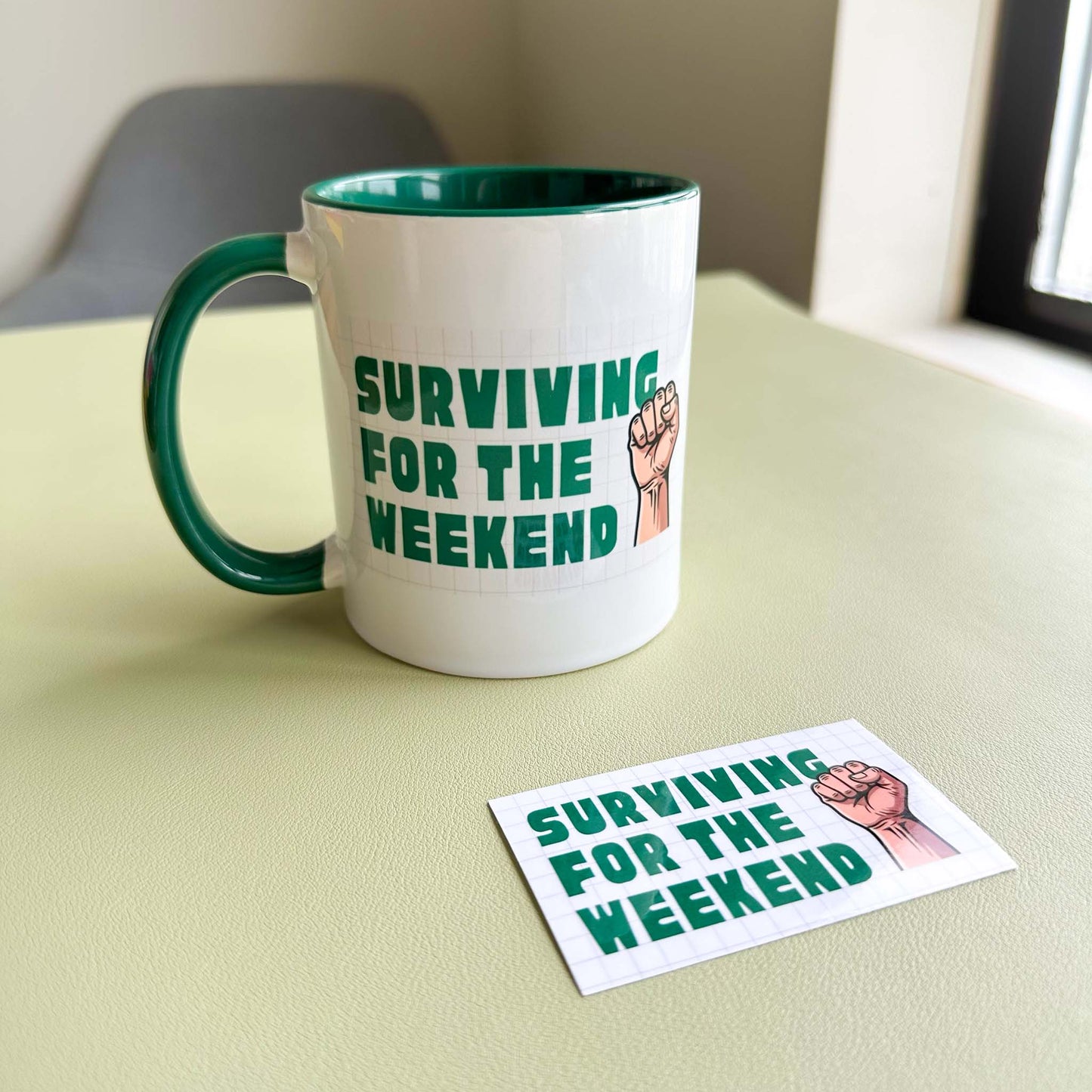 'Surviving for the weekend' ceramic mug paired with the matching vinyl sticker on a desk