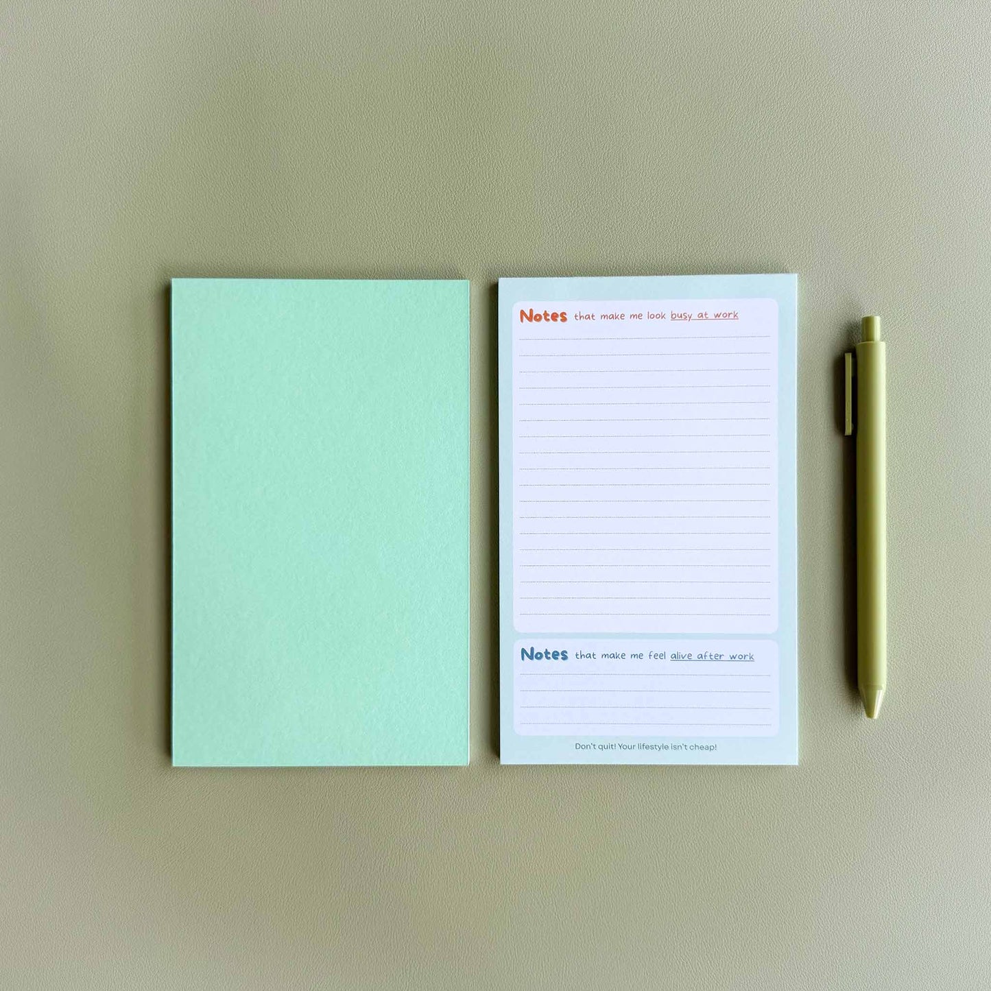 Two 'Busy at work, alive after work' dual-section notepads — one face up showing the dual 'Notes' layout and one face down showing the green back — beside a light green pen