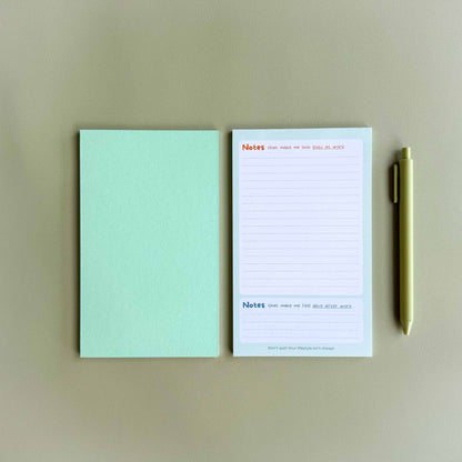Two 'Busy at work, alive after work' dual-section notepads — one face up showing the dual 'Notes' layout and one face down showing the green back — beside a light green pen