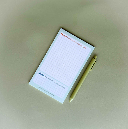 'Busy at work, alive after work' dual-section notepad on a desk with a light green pen beside it