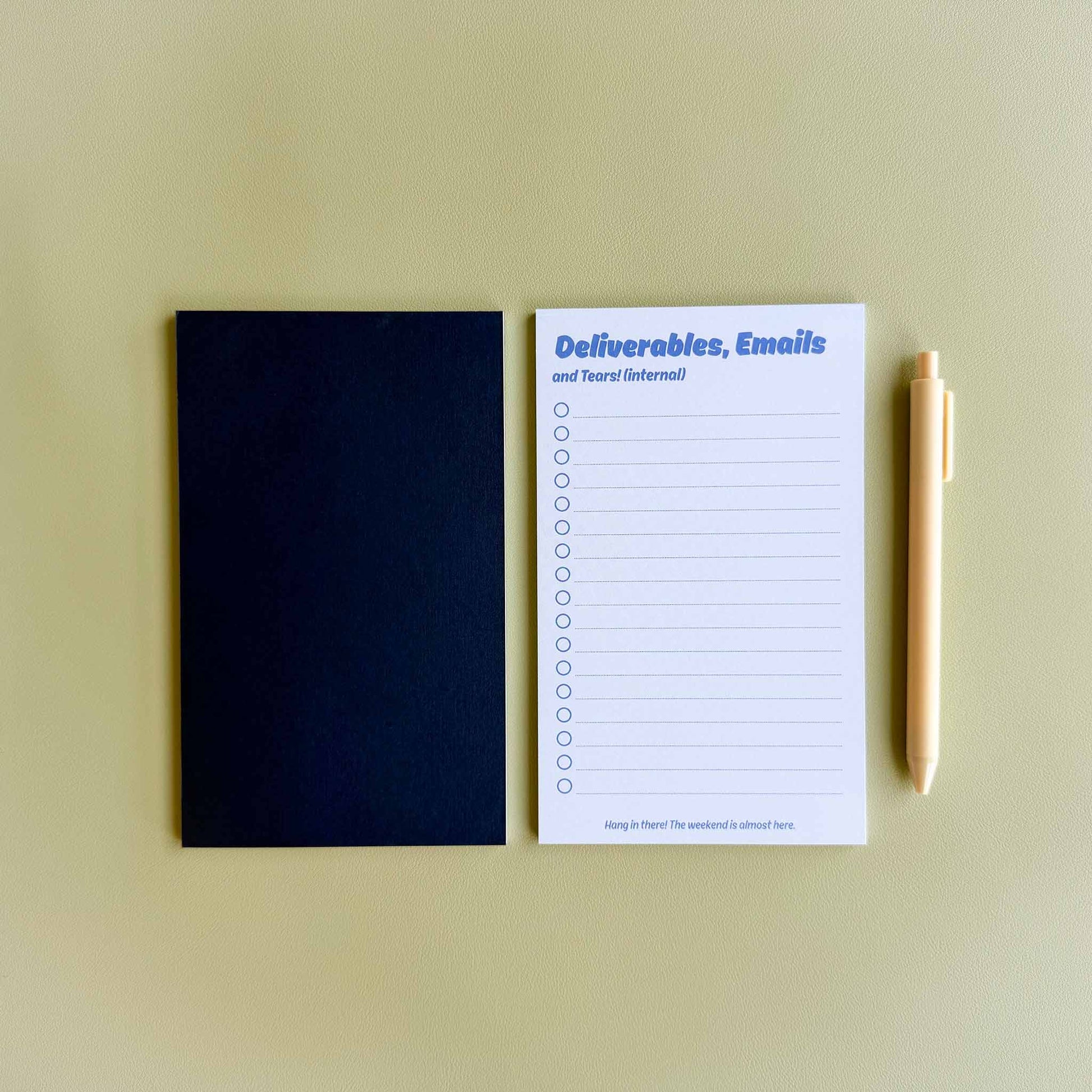 Two 'Deliverables, emails, and tears (internal)' to-do list notepads — one face up showing the checklist layout and one face down showing the dark blue back — beside a light yellow pen