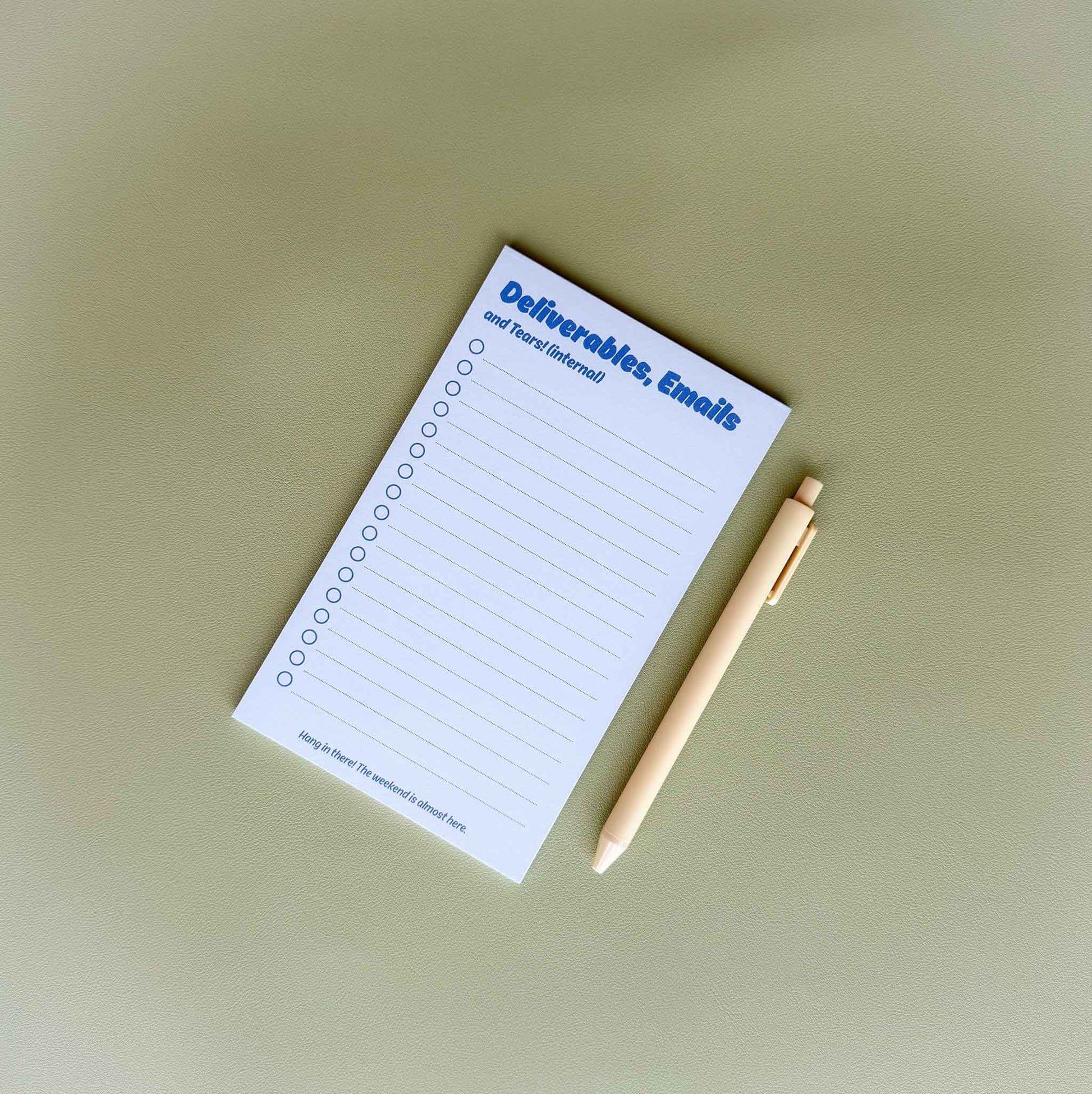 'Deliverables, emails, and tears (internal)' to-do list notepad on a desk with a light yellow pen beside it
